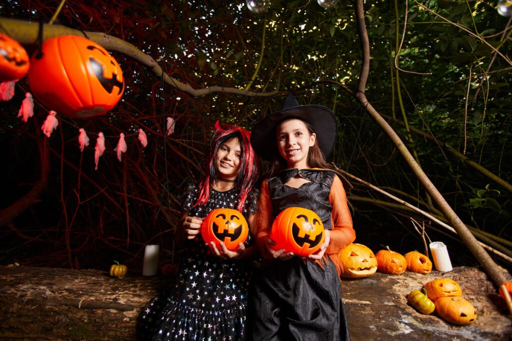 two girls in costumes holding toy pumpkins and smiling at camera they are at the party in the dark