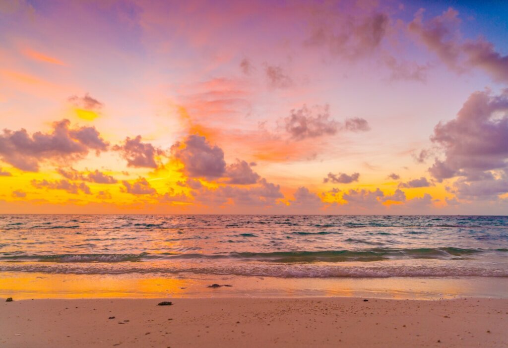 A colorful beach sunset with shades of pink, orange, and purple reflecting on the ocean waves.