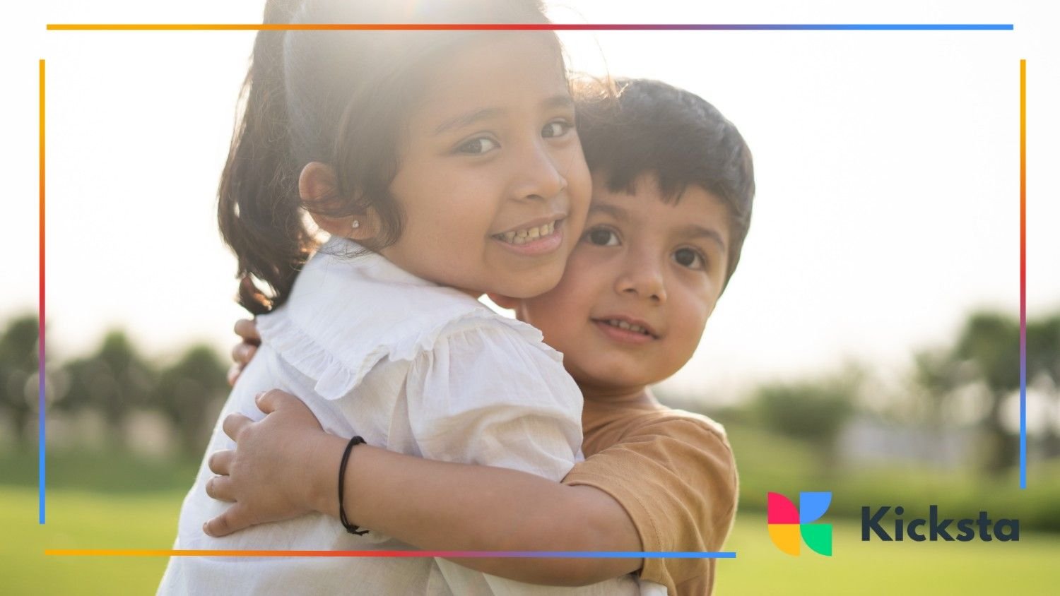 A young girl and boy smiling sweetly as they hug in a sunny park