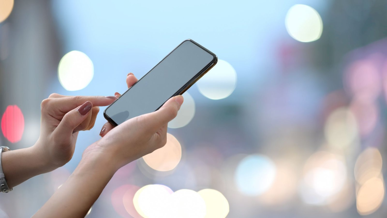 Close-up of a person using a smartphone outdoors with blurred city lights in the background.