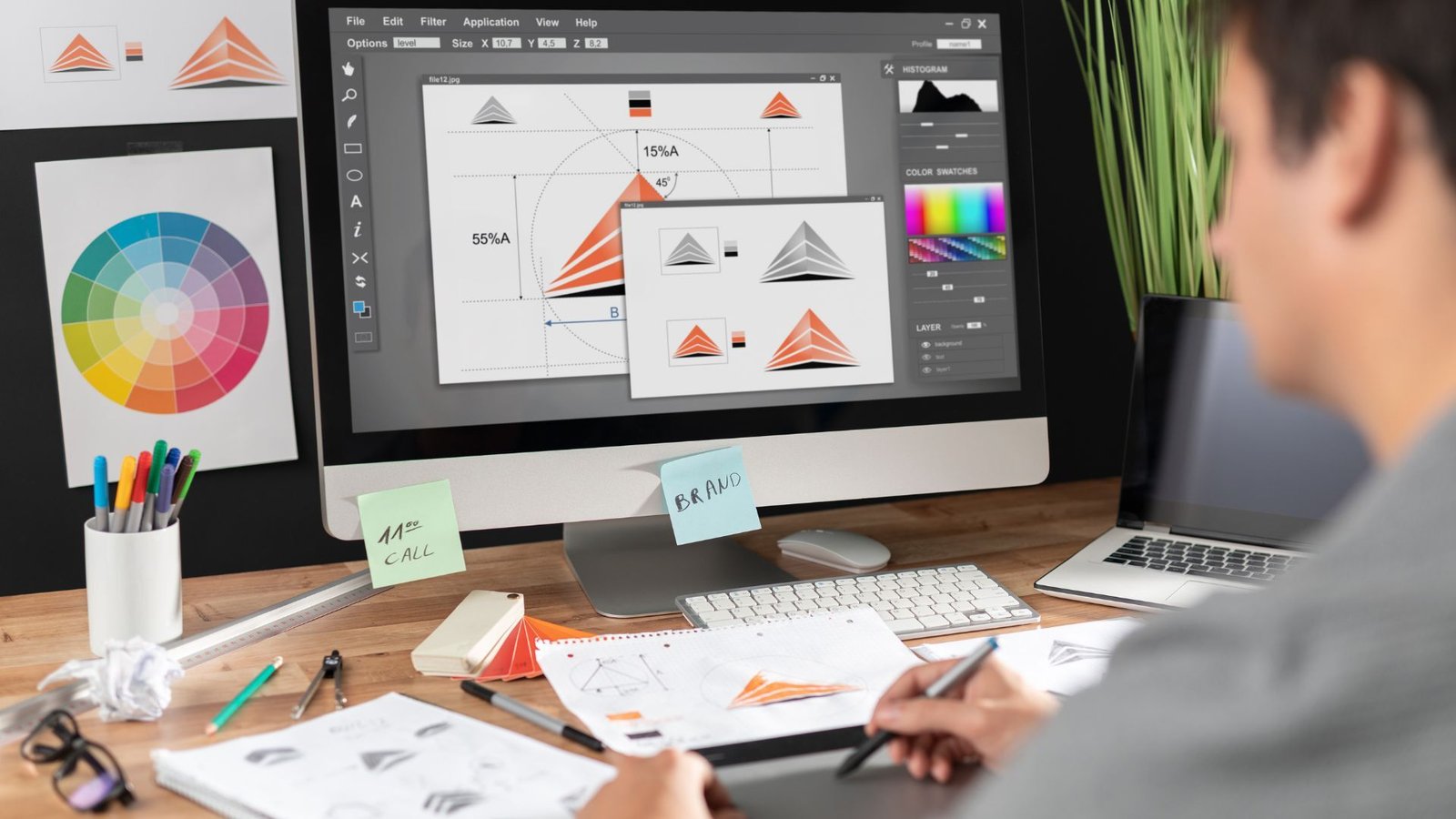 Graphic designer creating a logo on a computer, surrounded by sketches and color palettes.
