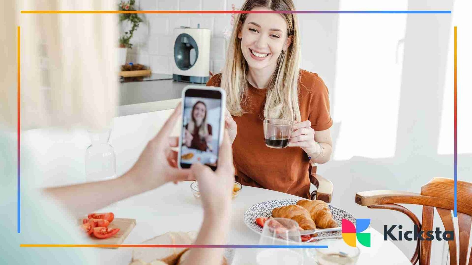 Woman smiling while being filmed on a phone at a breakfast table.