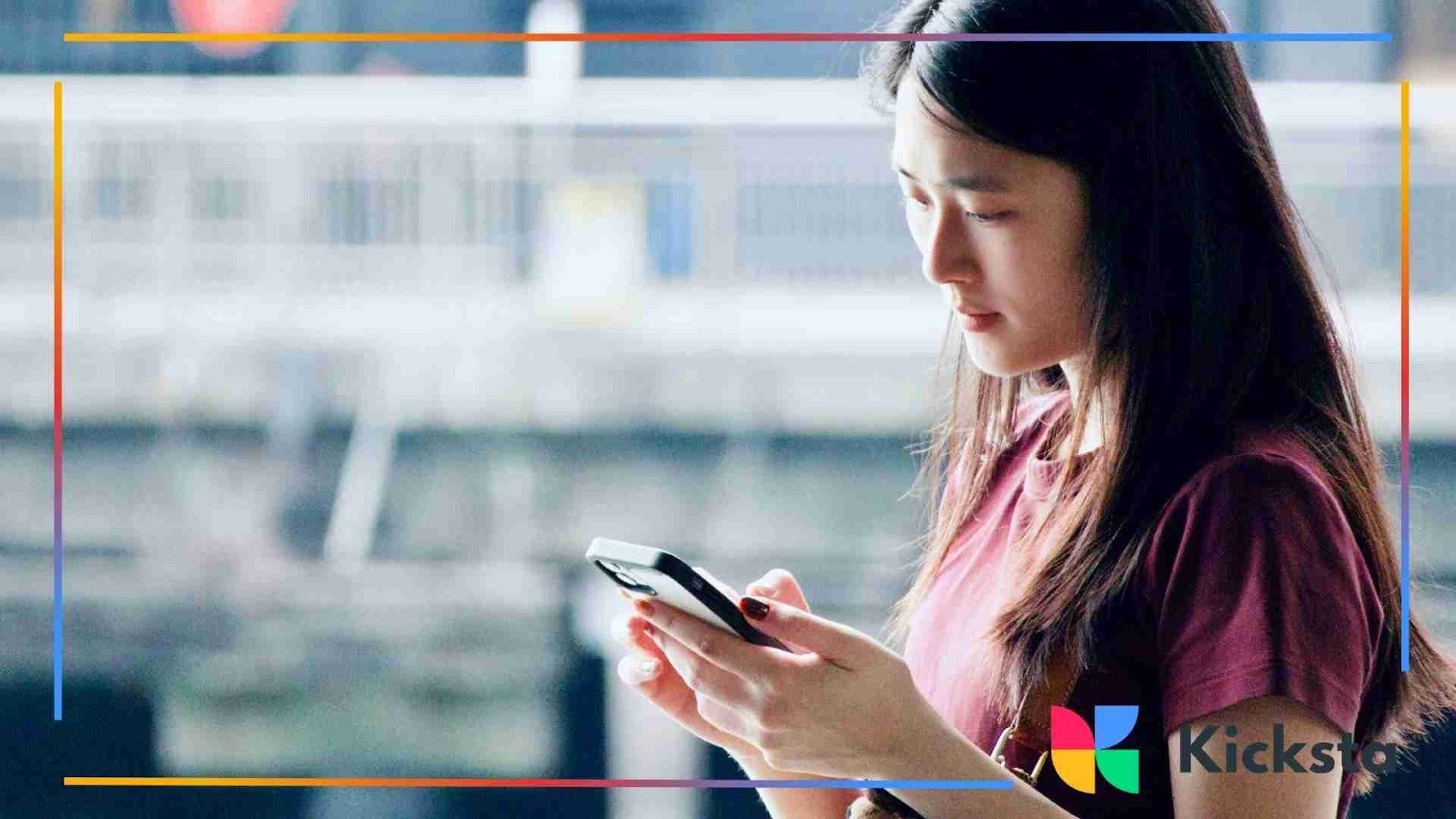 A young woman standing outside and focused on her smartphone, holding it with both hands.