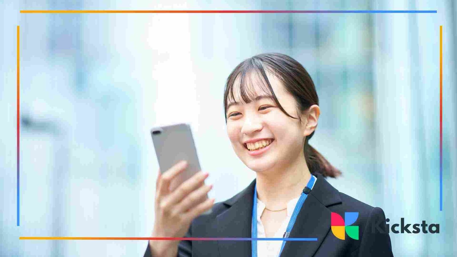 Smiling young woman in a business suit looking at her smartphone while standing outdoors in a bright, modern city setting.