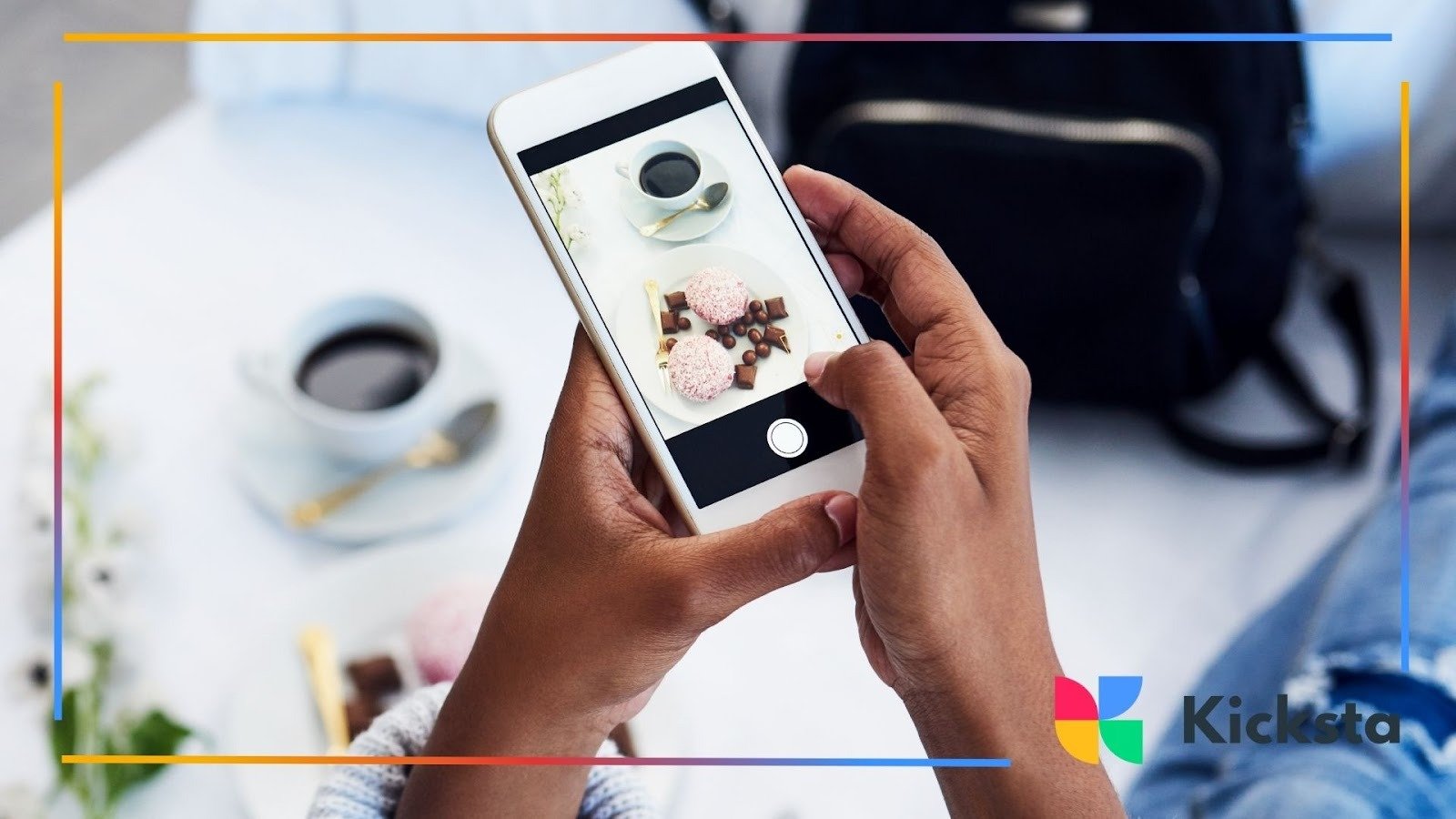 Person taking a photo of a coffee cup and dessert setup using their smartphone, with the scene arranged on a white surface.