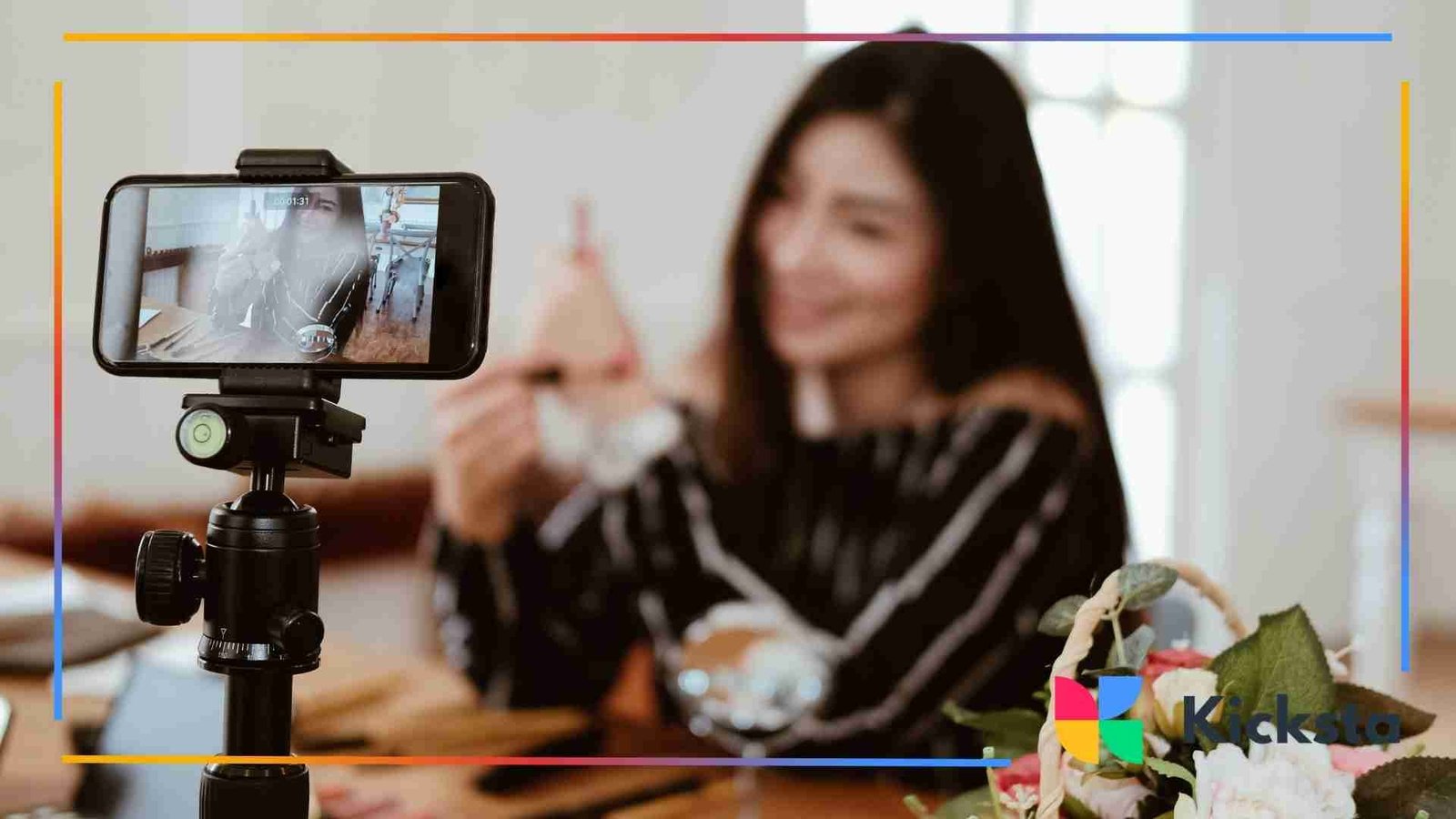 Woman recording a video on her smartphone mounted on a tripod while holding a product and smiling.