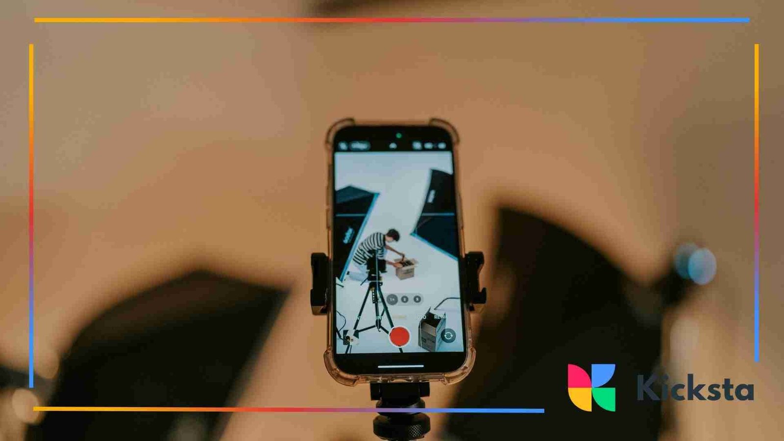 A smartphone mounted on a tripod recording a person arranging products in a photography studio setup.