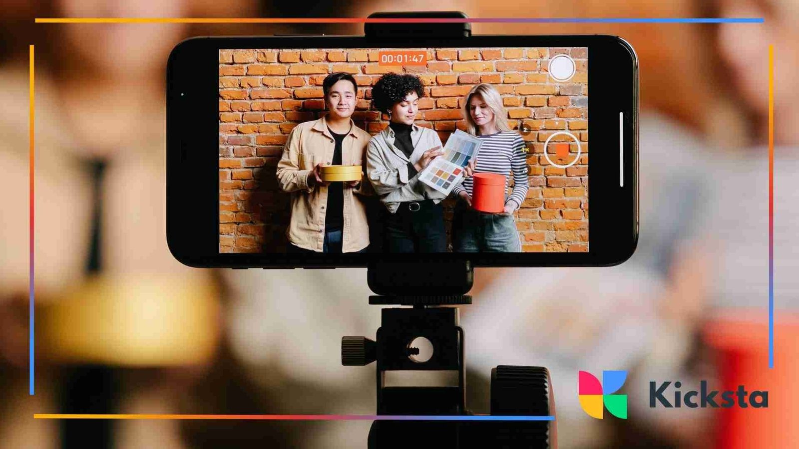 A smartphone on a tripod recording three people standing against a brick wall, holding props and presenting to the camera.