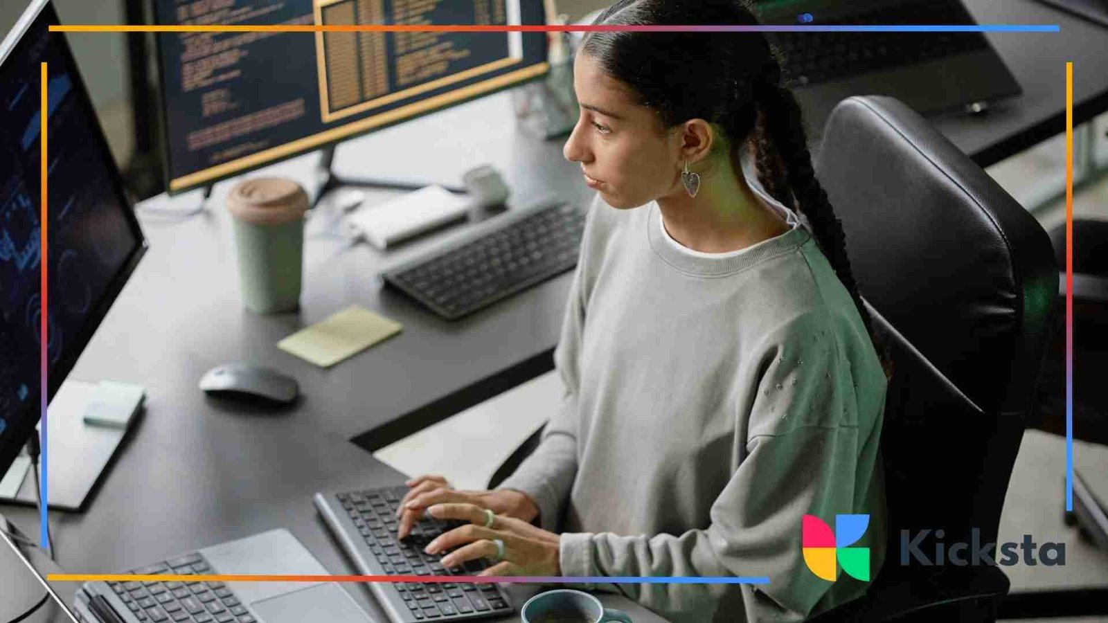 A woman typing at a desk with multiple computer monitors displaying code and data, focusing intently on her work.