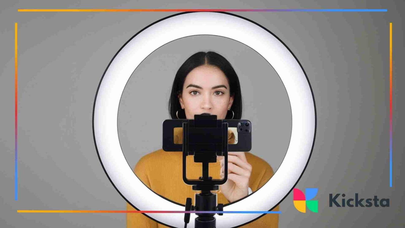Woman standing behind a ring light, recording herself with a smartphone placed in the center of the light.