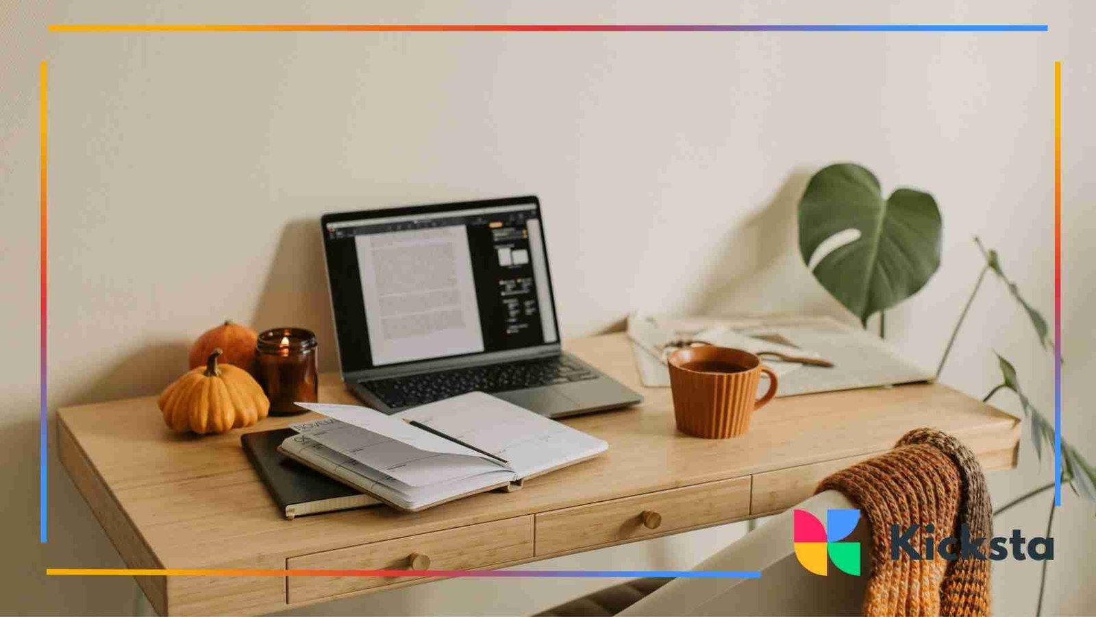 Cozy home workspace with a laptop, notebooks, coffee mug, pumpkins, and a knitted blanket draped over a chair.