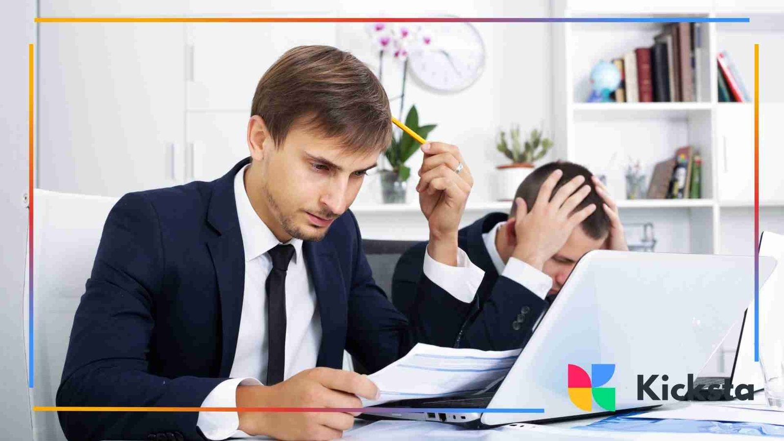 Two businessmen sitting at a desk looking stressed; one reviews documents while the other holds his head in frustration near a laptop.
