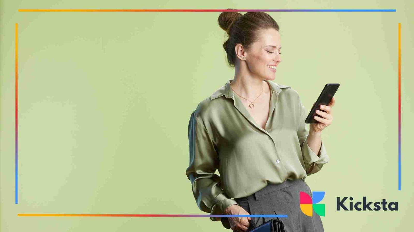 Woman standing against a green background smiling while looking at her phone.