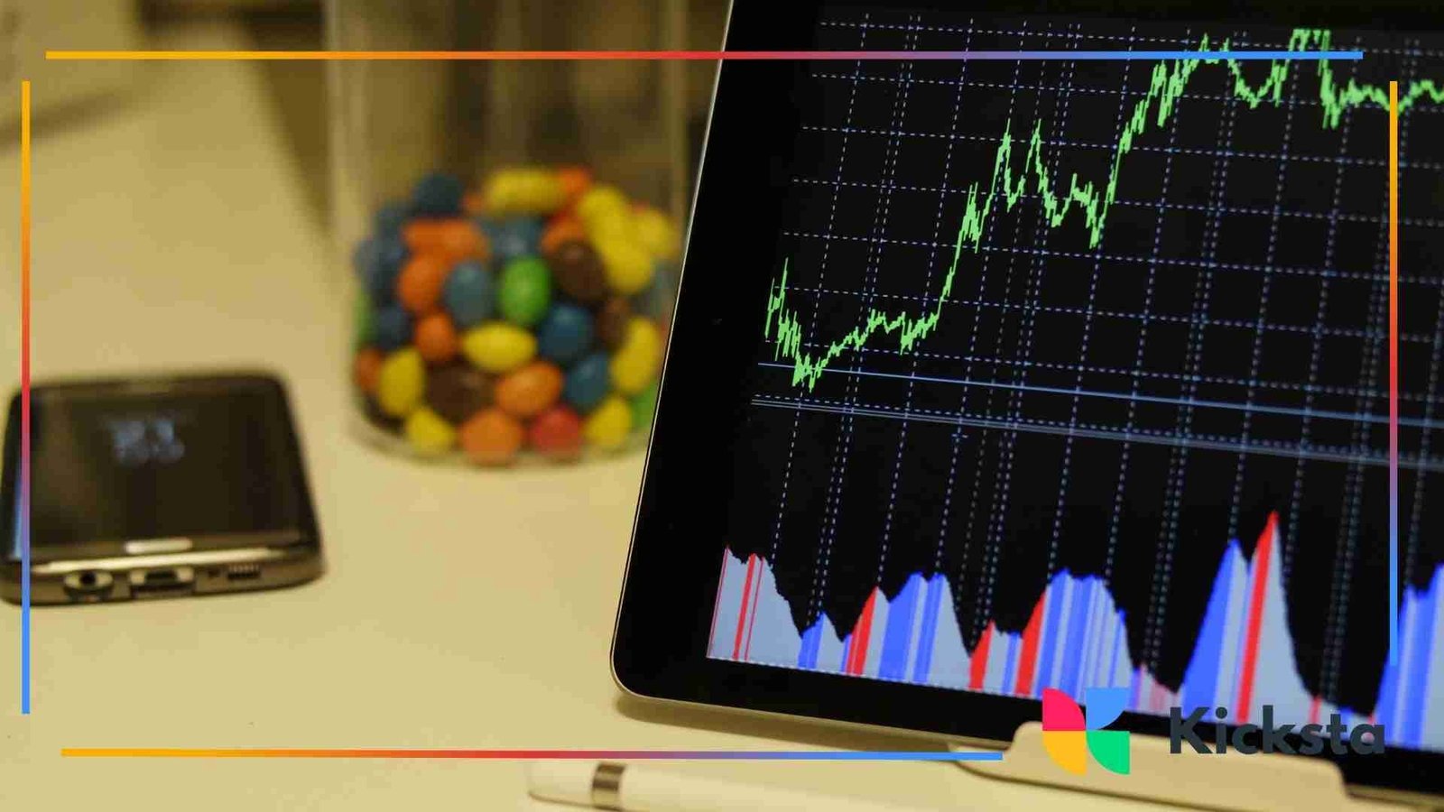 Tablet displaying a rising line graph on a dark screen, placed beside a jar of colorful candy and a smartphone.