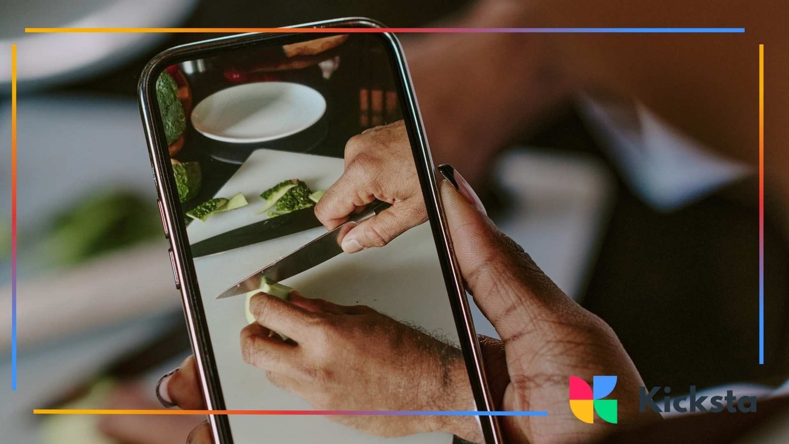 Hands holding a smartphone while recording a close-up video of someone chopping vegetables in a kitchen.