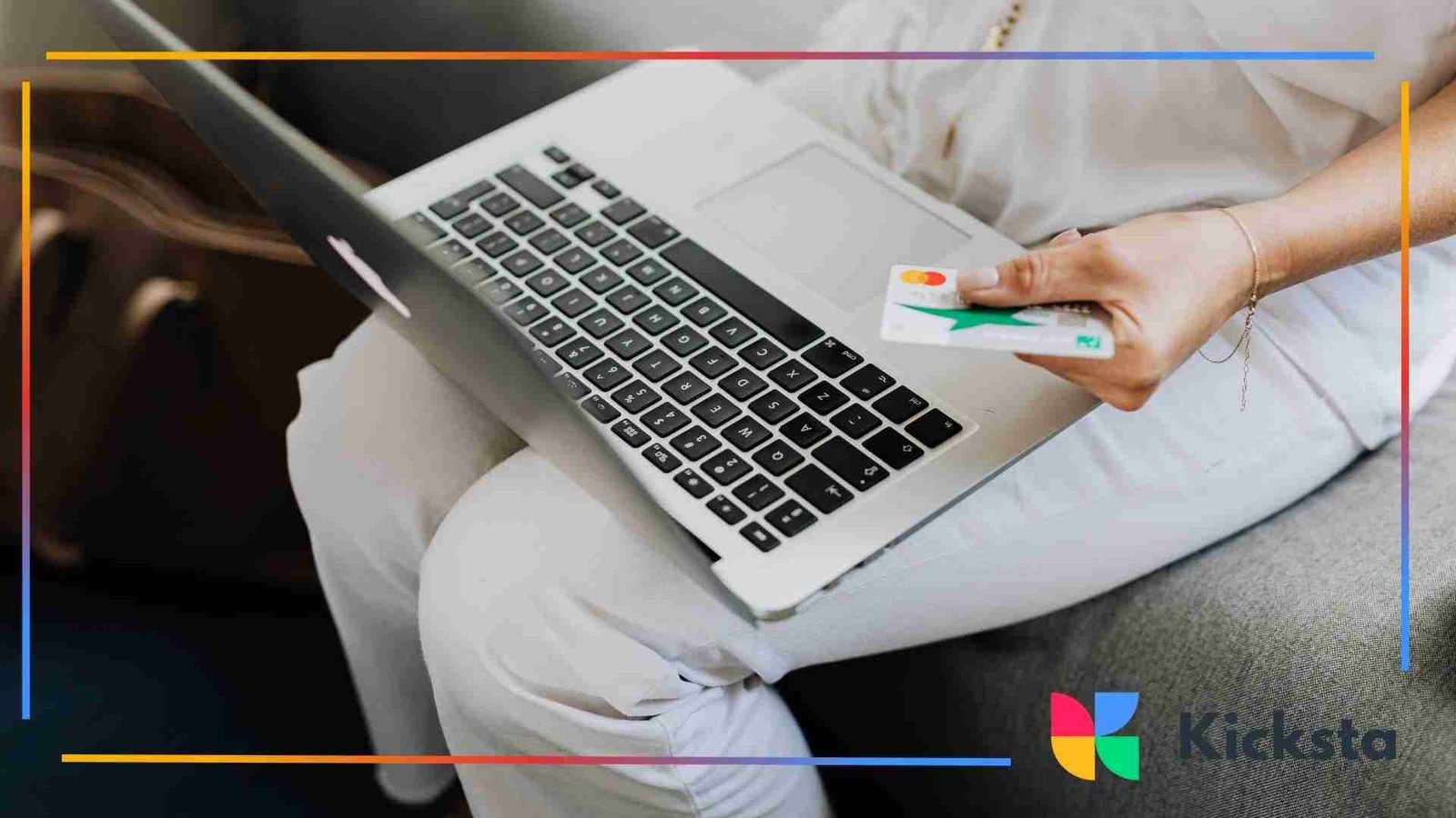 Person holding a credit card while using a laptop on their lap, shopping online from home.