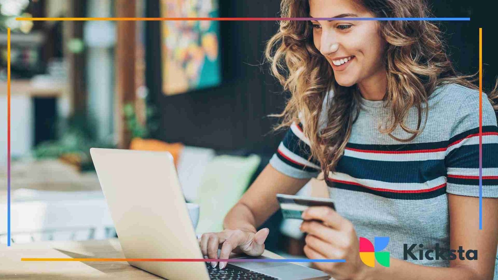 Woman smiling while entering credit card information on her laptop in a cozy café setting.