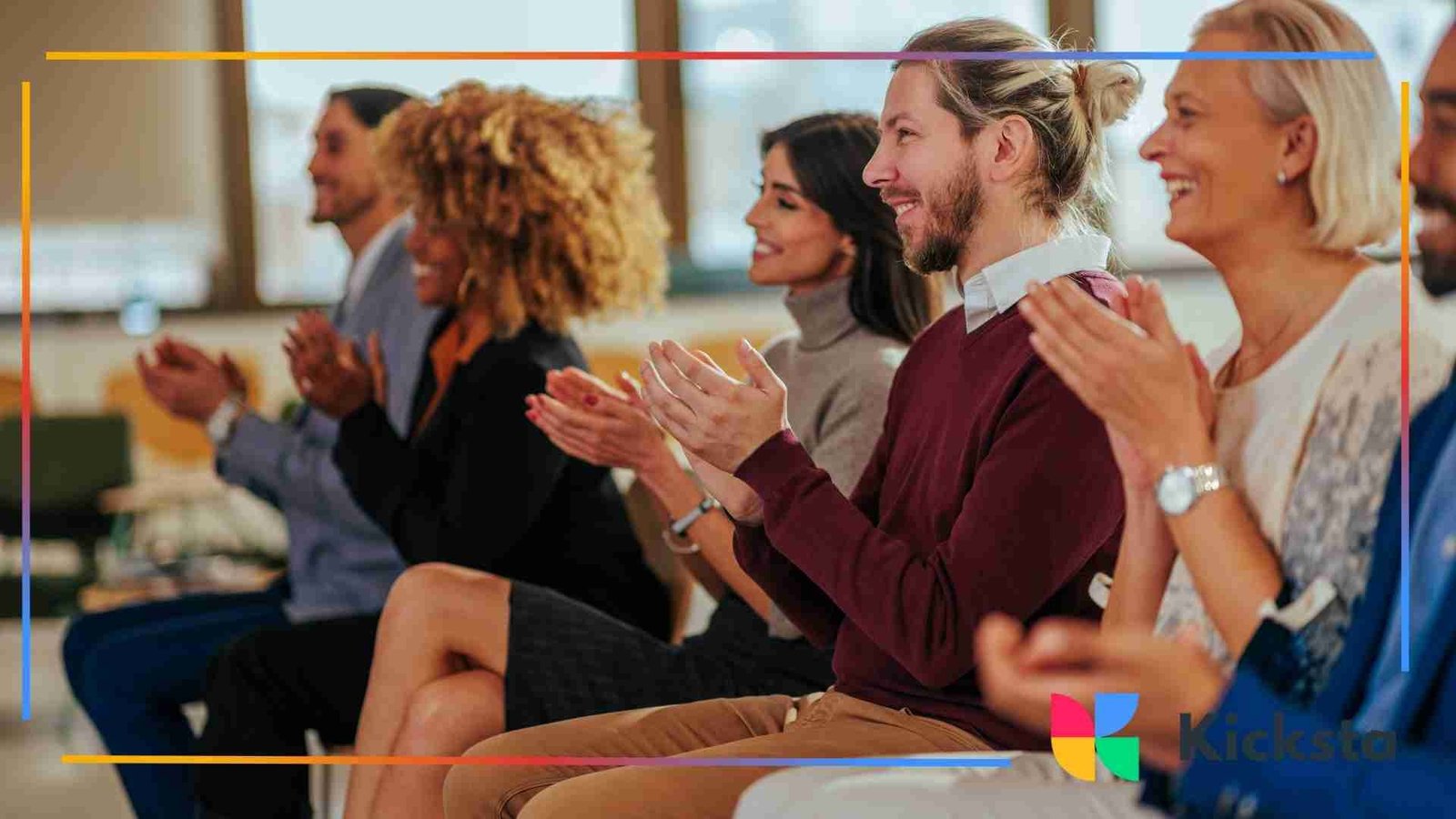Group of diverse people sitting in a row at an event, smiling and applauding with enthusiasm.