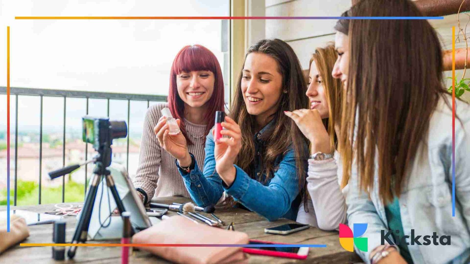 Four young women sitting together outdoors, holding and showing nail polish bottles while recording a beauty video with a camera on a tripod.
