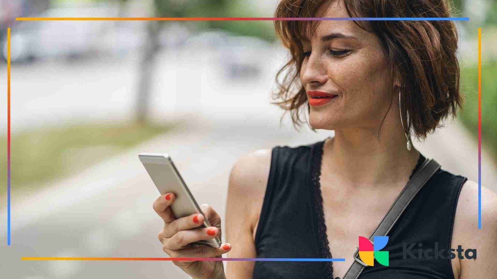 A woman outdoors looking at her smartphone with a slight smile on her face.
