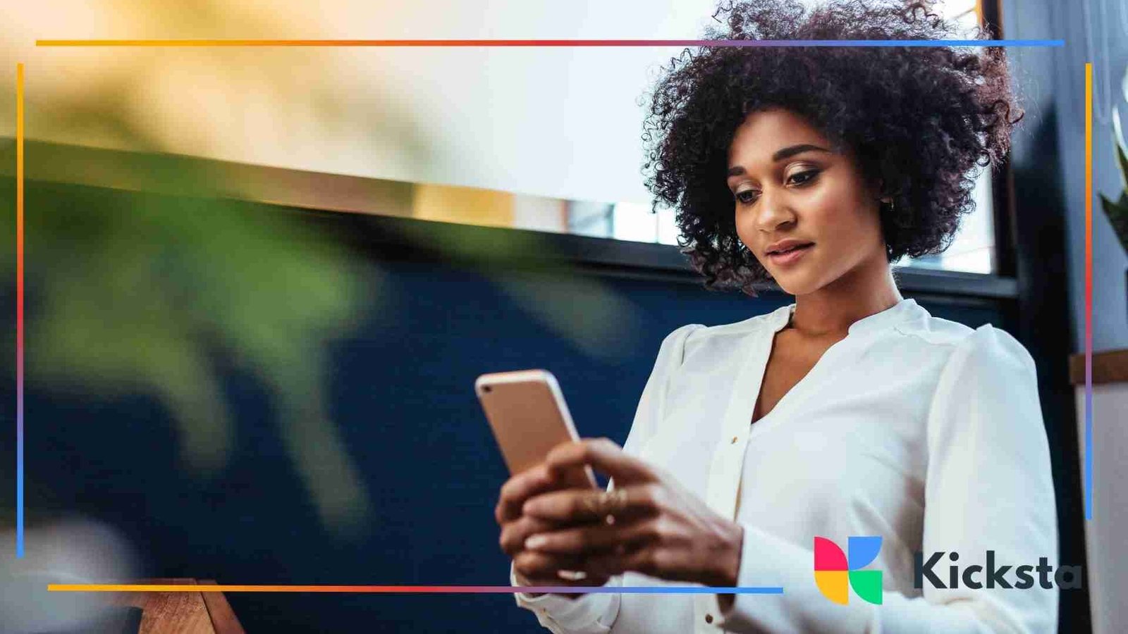 A woman with curly hair looking at her phone while sitting indoors, appearing focused and relaxed.