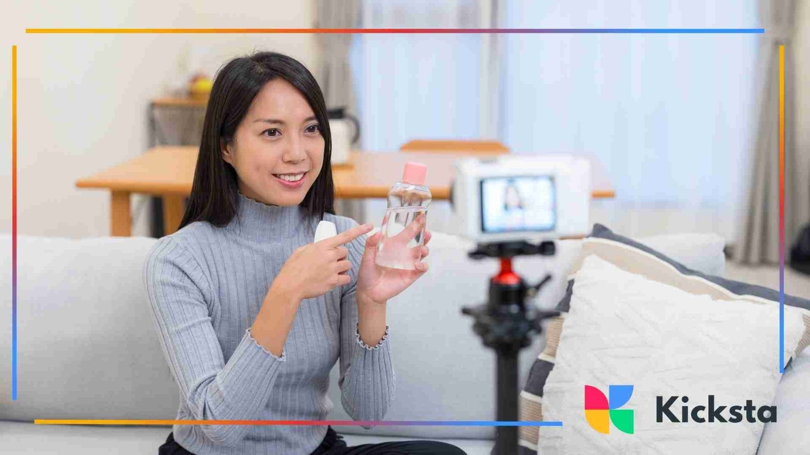 Woman sitting on a couch pointing at a clear bottle while recording a video with a camera setup.