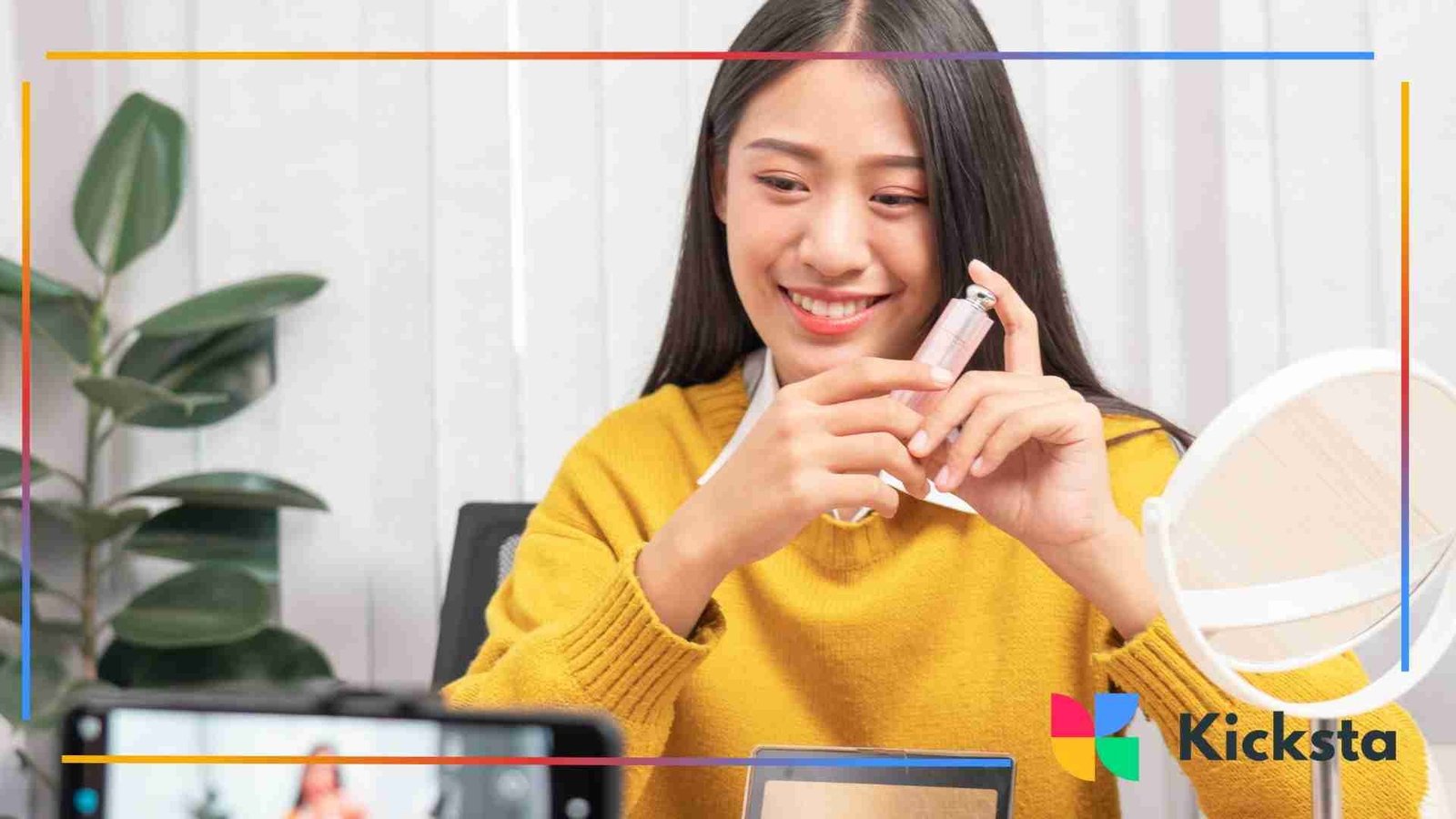Woman recording a beauty video while holding a cosmetic product in front of a camera at her desk.