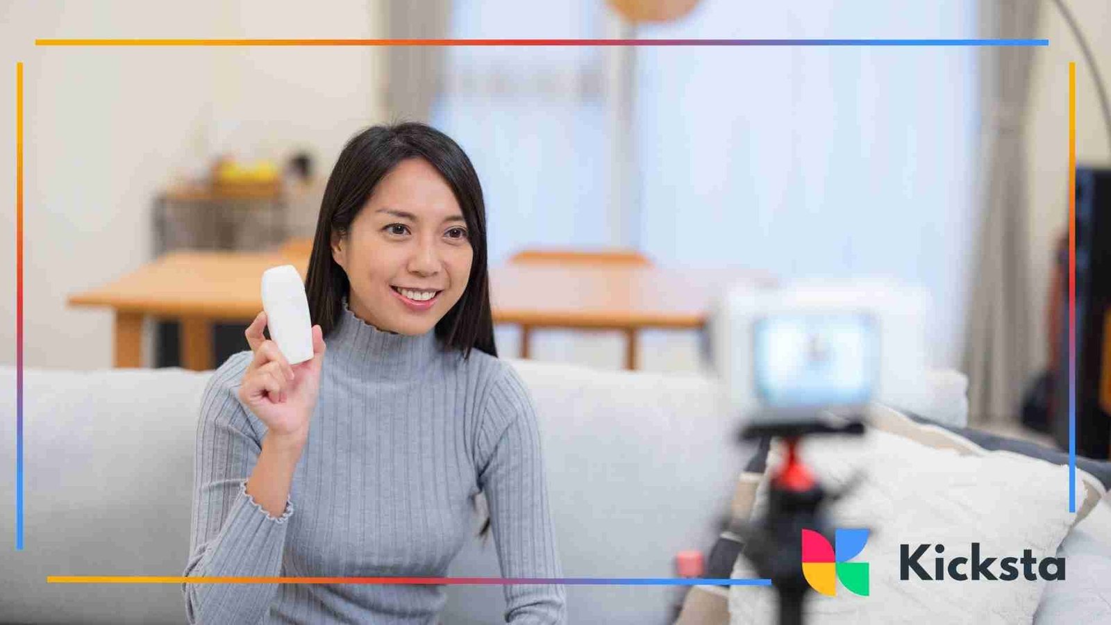 Woman sitting on a couch recording a product review video while holding up a white item toward her camera.
