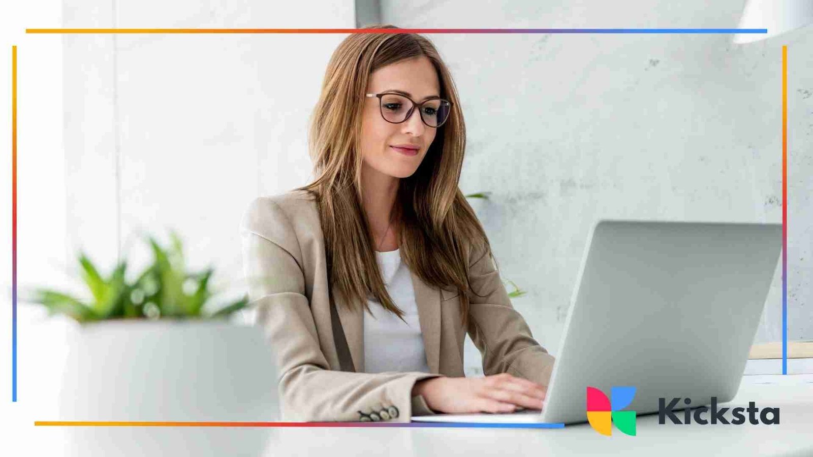 Professional woman wearing glasses working on a laptop at a clean desk in a bright office.