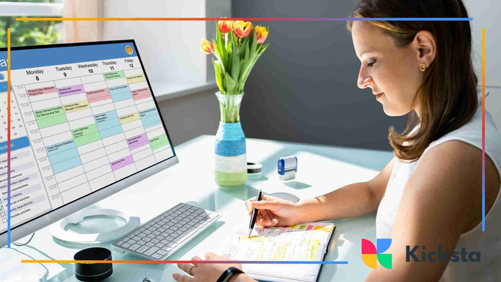 Woman writing notes at a desk while reviewing a color-coded digital calendar on a computer screen.