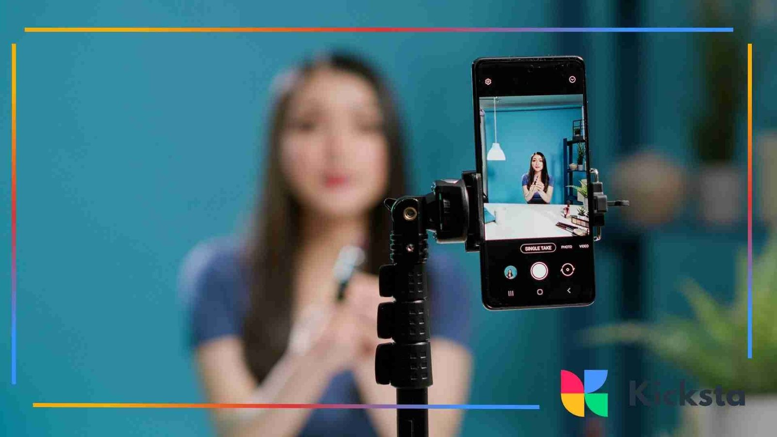 Smartphone mounted on a tripod recording a woman speaking in front of a teal background.