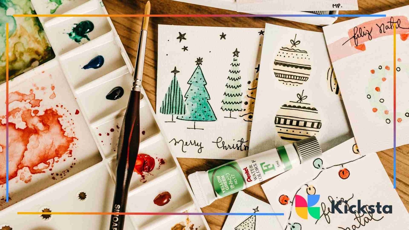 Hand-painted Christmas cards featuring trees and ornaments surrounded by watercolor paints, brushes, and art supplies.