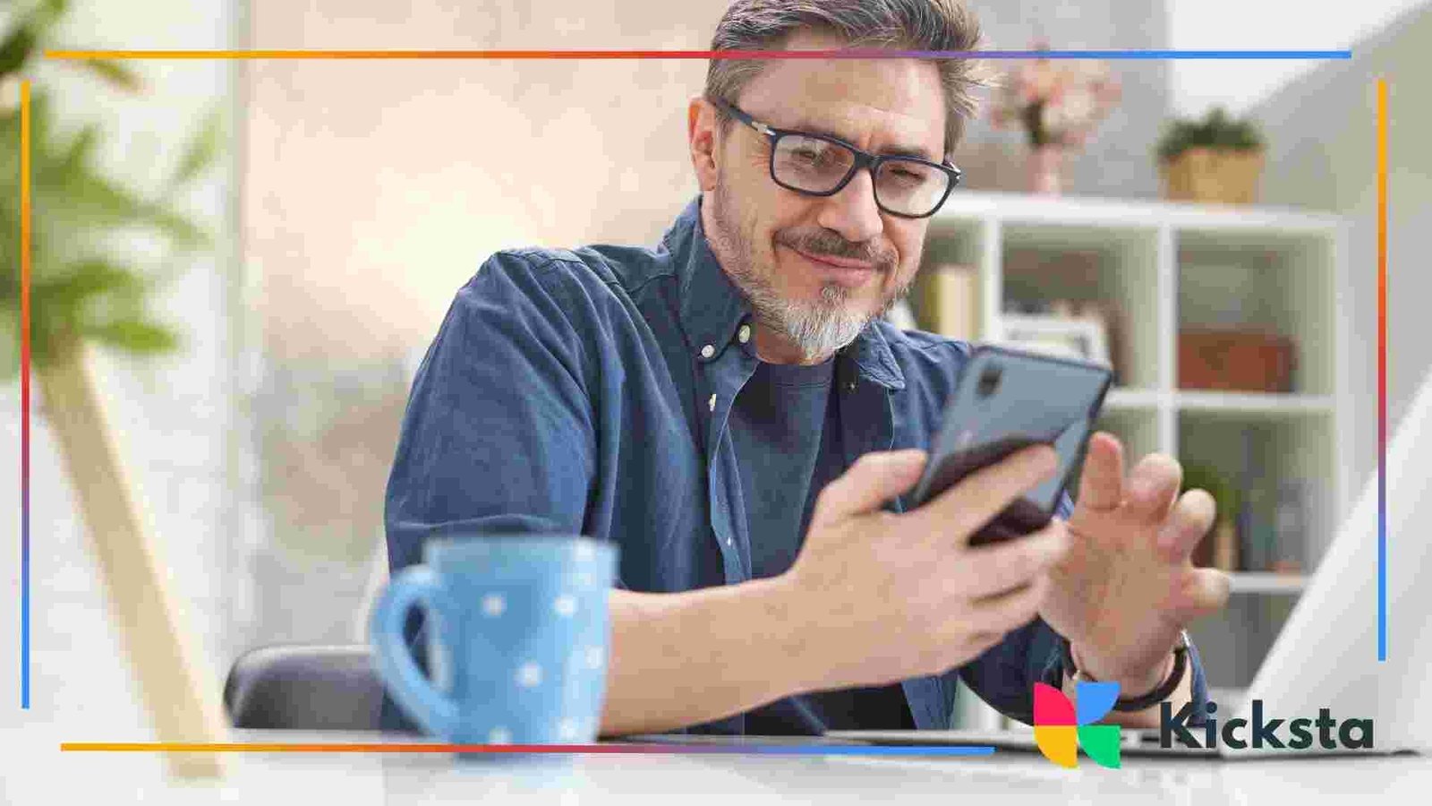 Person wearing glasses using a smartphone while sitting at a desk with a coffee mug and laptop nearby.